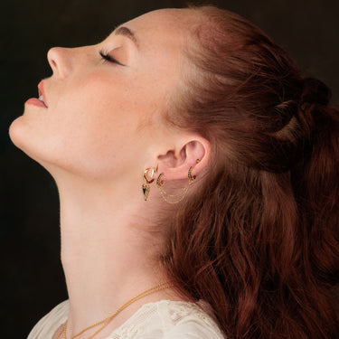 Woman Wearing Gold Black Stone Huggie Hoop Earrings with Double Chain Connector in Third Lobe and Upper Ear Piercing
