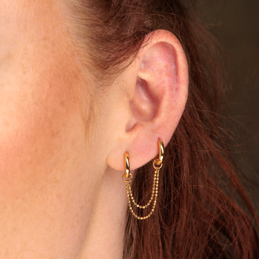 Gold Huggie Hoop Earrings with Twin Chain Connector worn in first and second ear lobe piercings