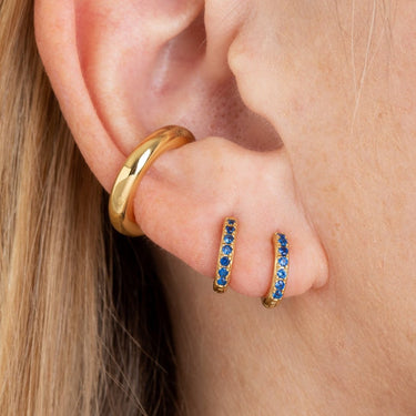 Gold Huggie Earrings with Blue Stones on Model's Ear can be worn in lobe or cartilage piercings
