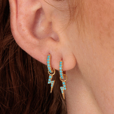 Pair of gold lightning bolt charm hoop earrings in ear lobe