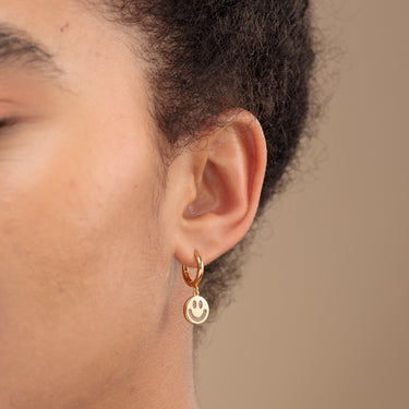 Woman Wearing Gold Charm Hoop Earrings with Smiley Face Charm Studded with Clear CZ Stones