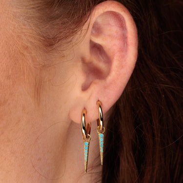 Woman wearing gold turquoise spike charm hoops in first and second ear lobe piercing