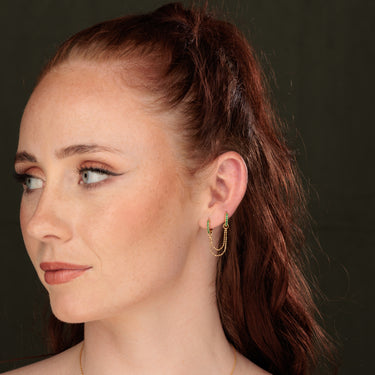 Woman Wearing Emerald Green Double Huggie Earring with Twin Chain Connector in Gold
