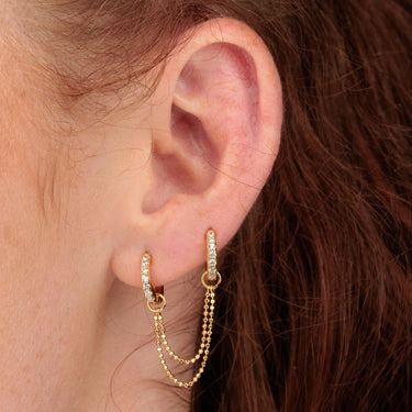 Ear Close up of Gold Clear Stone Huggie Hoop Earrings with Double Chain Connector