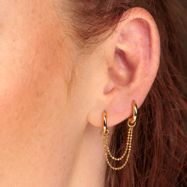 Woman Wearing Gold Huggie Earrings with Twin Chain Connector in multiple ear lobe piercings