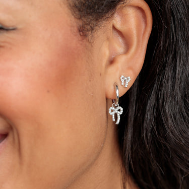Silver bow earrings shown in lobe piercings on model